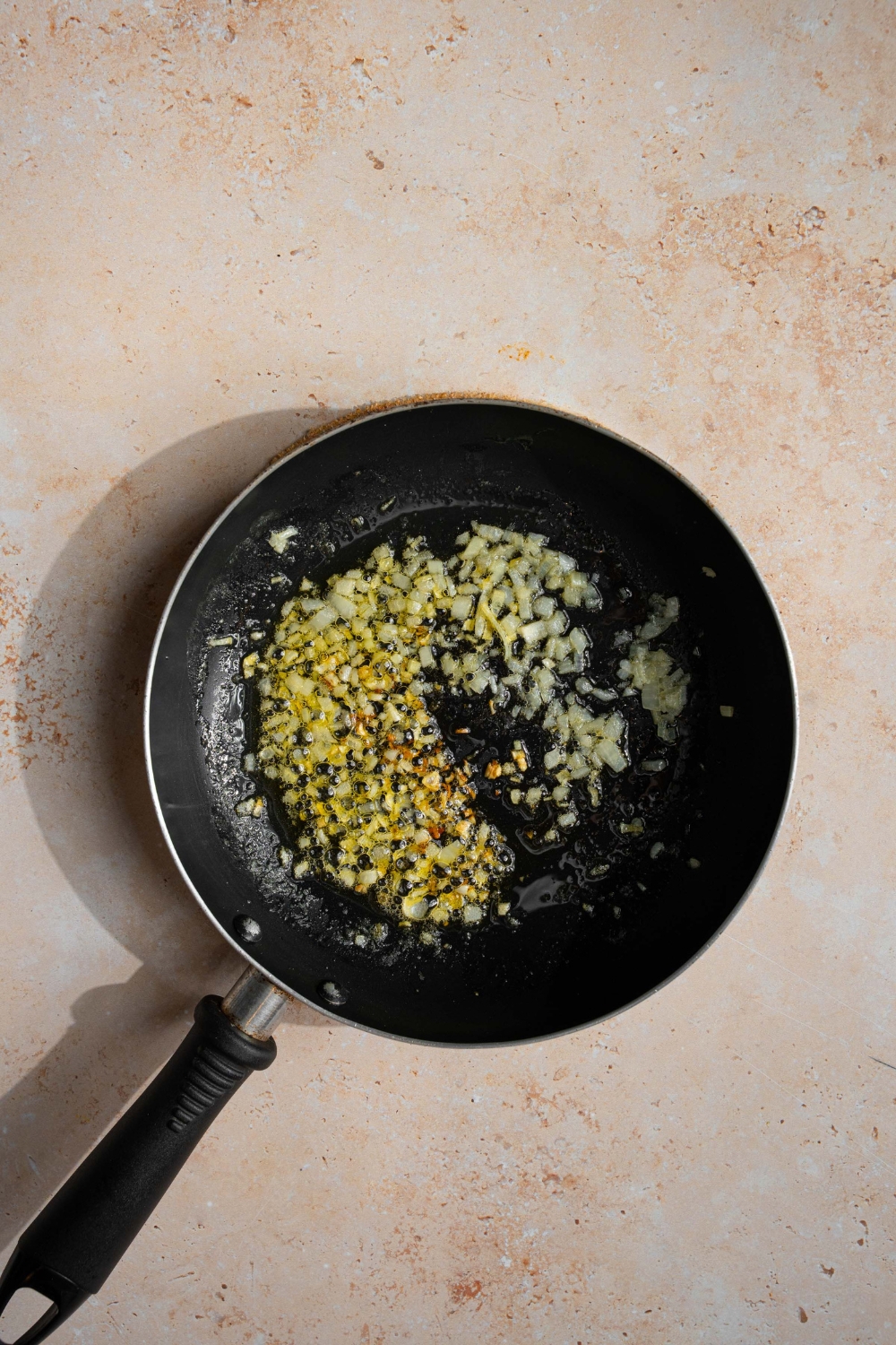 A skillet with diced shallots cooking in butter. The skillet is on a tan counter.