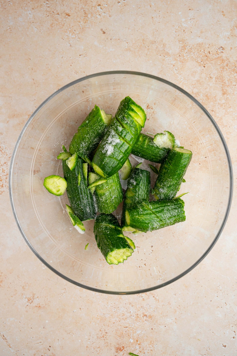 A glass bowl with spiraled cucumbers tossed in salt. The bowl is on a tan counter.