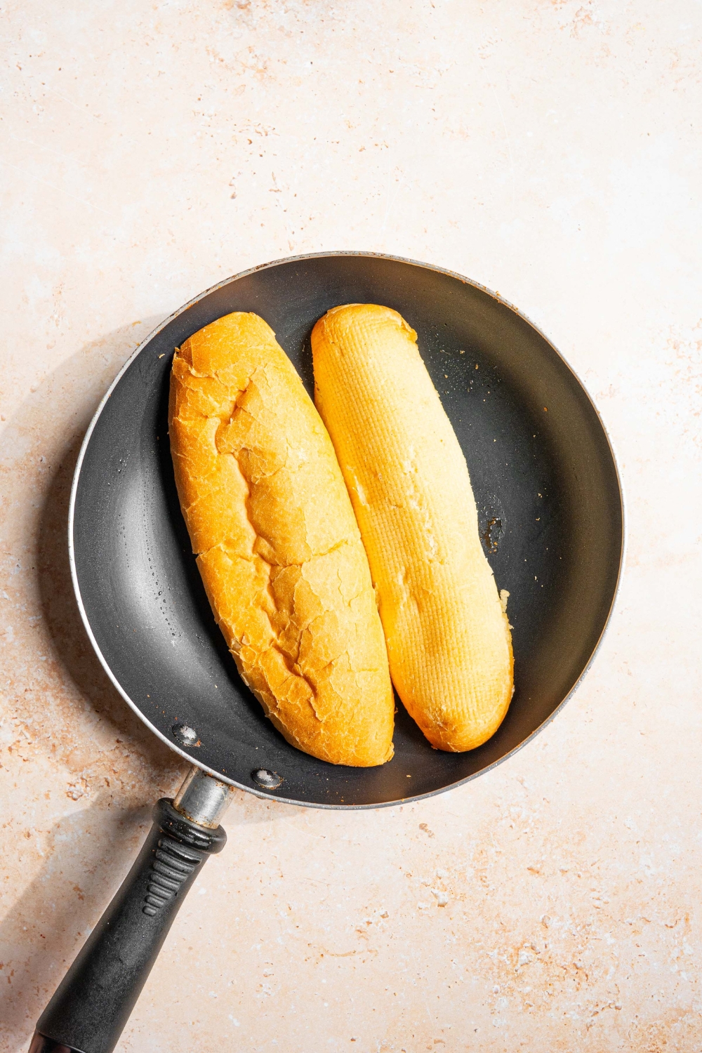 A skillet with a sliced bread loaf laying face down. The skillet is on a tan counter.