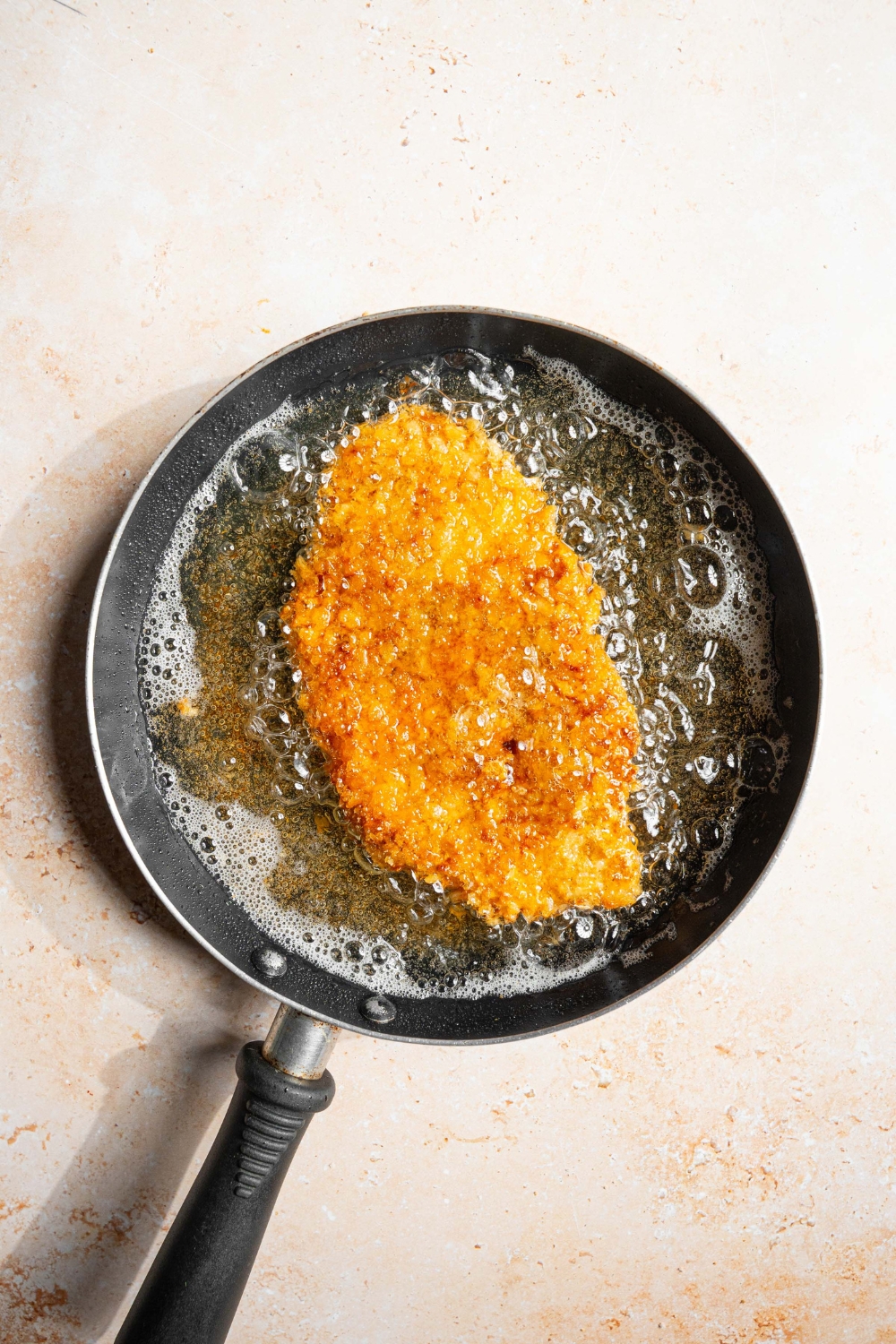 A skillet with a breaded chicken cutlet frying in oil.