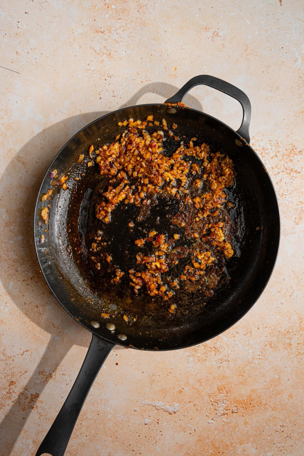 A skillet with sautéed onion and garlic. The skillet is on a tan counter.