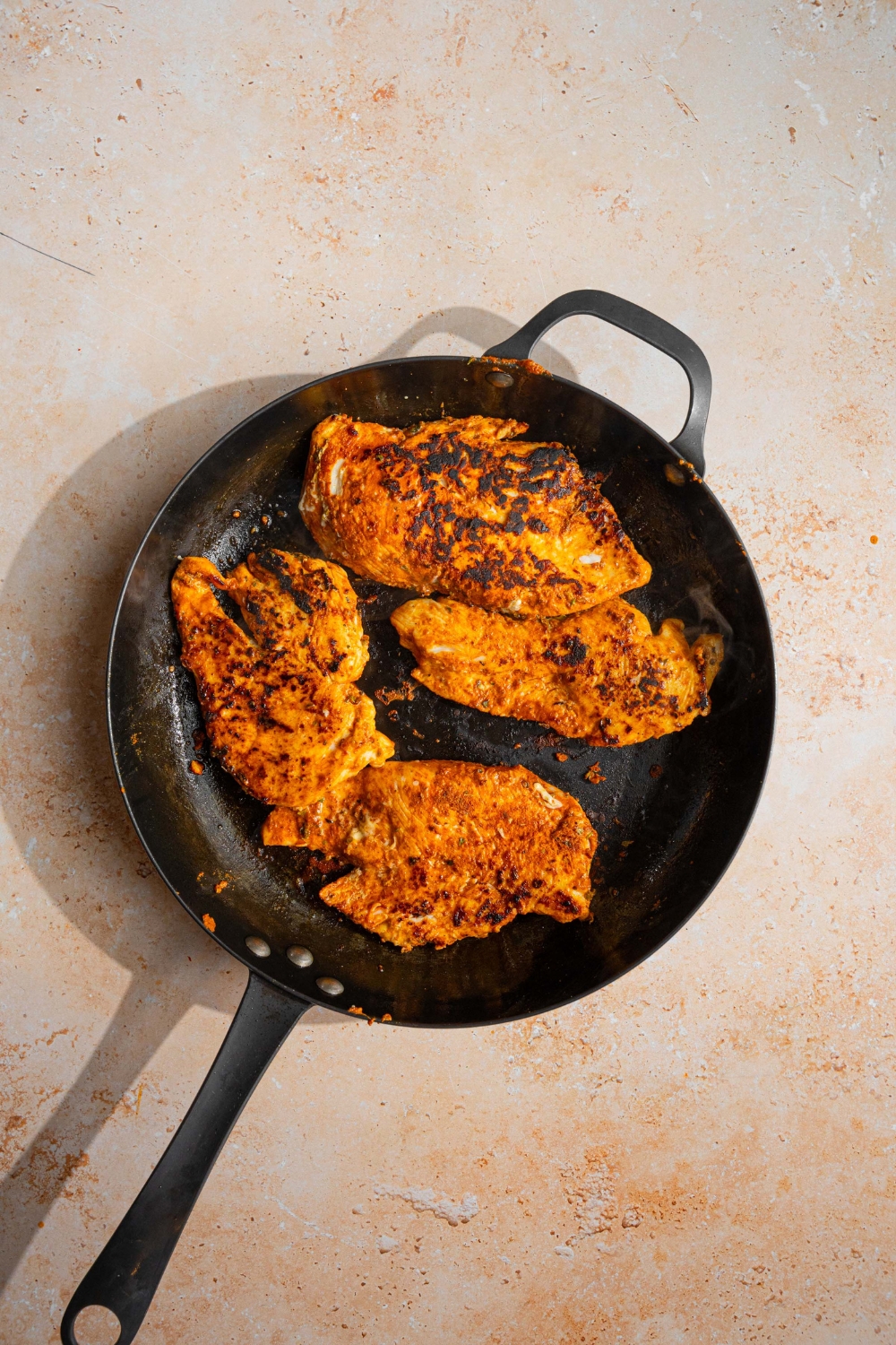 A skillet with seasoned chicken cooked on both sides. The skillet is on a tan counter.