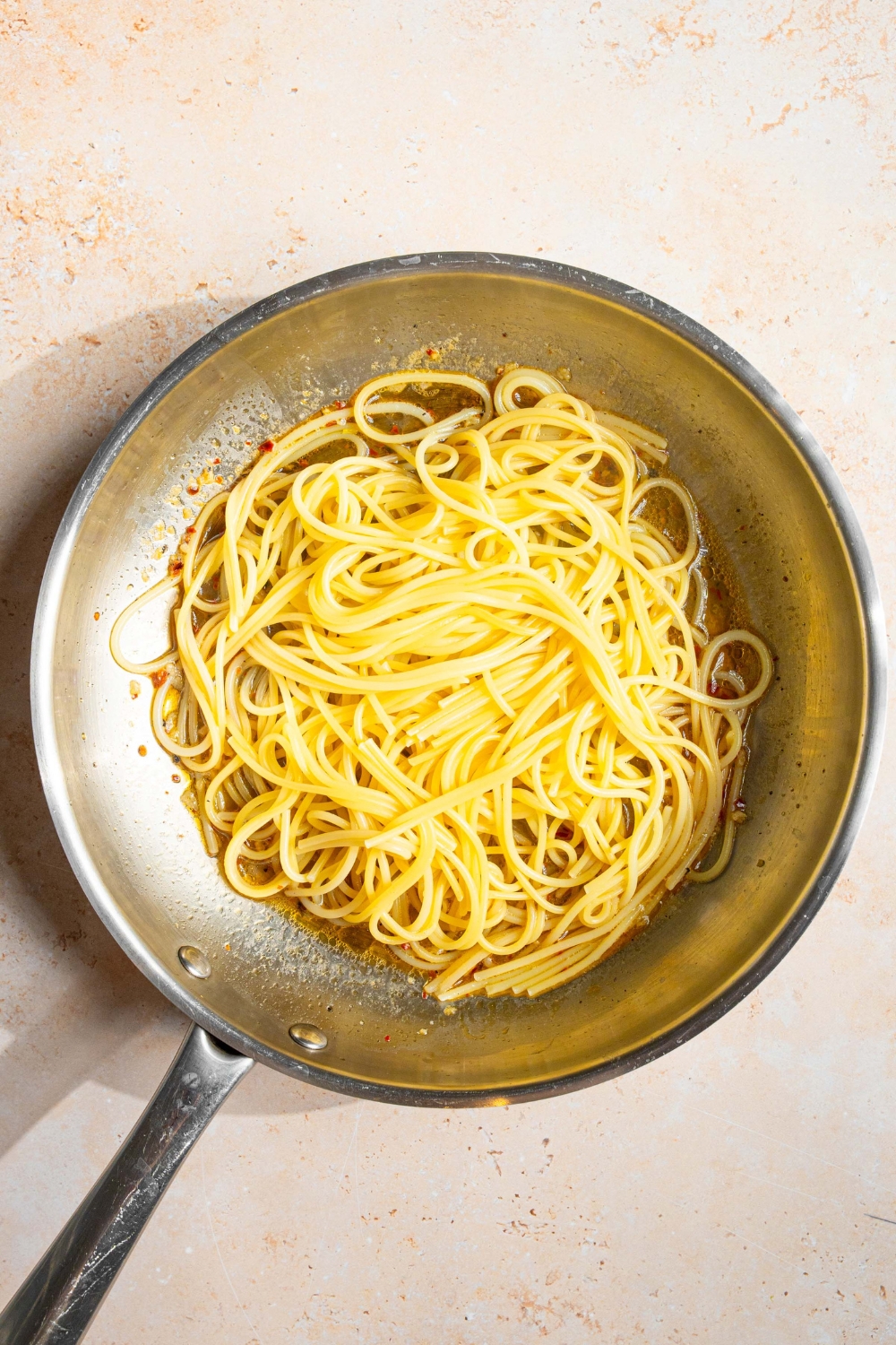 A skillet with white wine sauce with spaghetti on top. The skillet is on a tan counter.