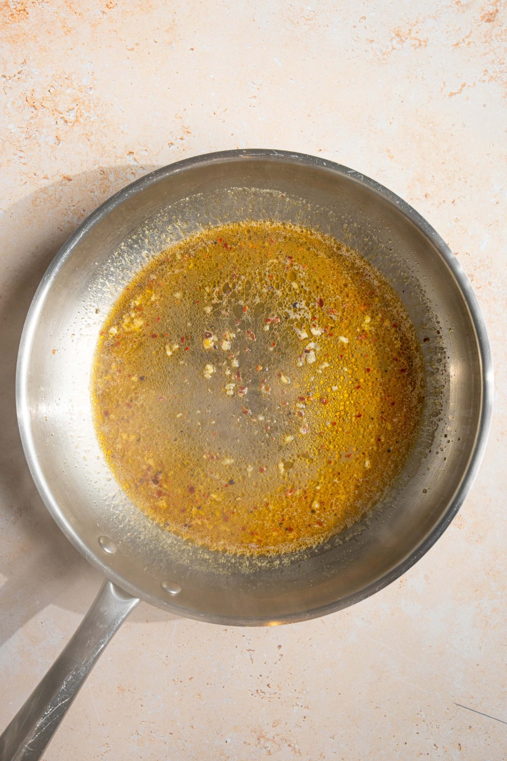 A skillet with melted butter in a white wine sauce. The skillet is on a tan counter.