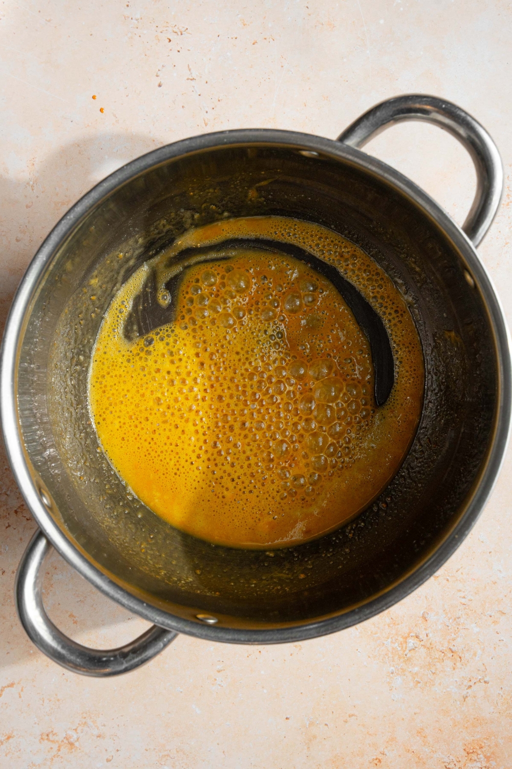 A pot with seasonings mixed with a roux. The pot is on a tan counter.