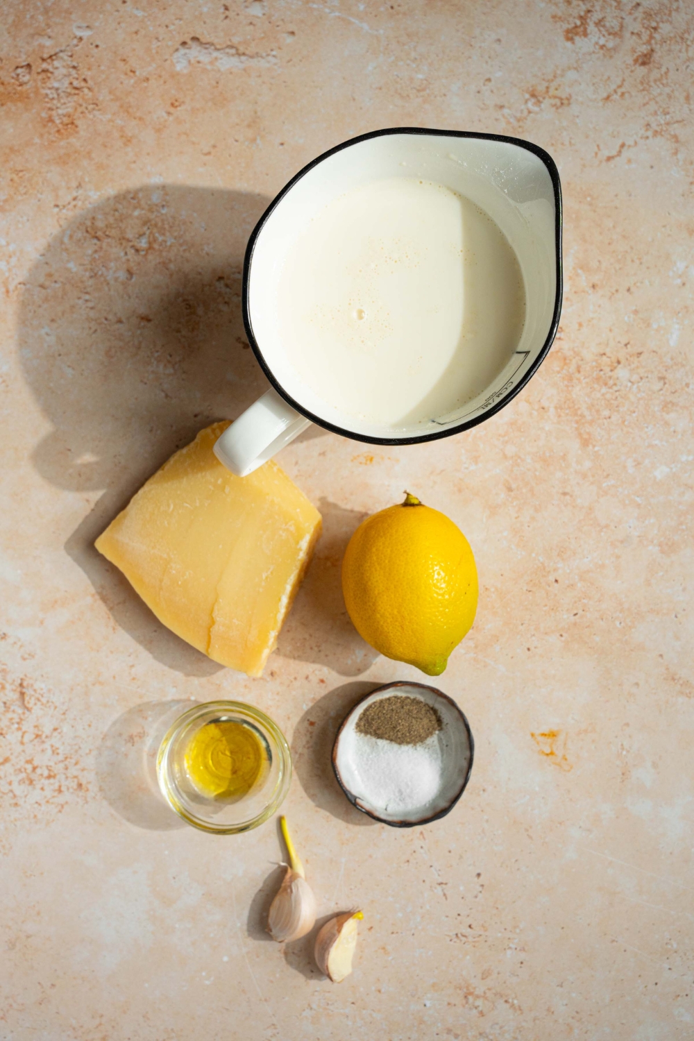 An overhead shot of ingredients to make lemon cream sauce including heavy cream, a lemon, olive oil, garlic, seasonings, and parmesan cheese.