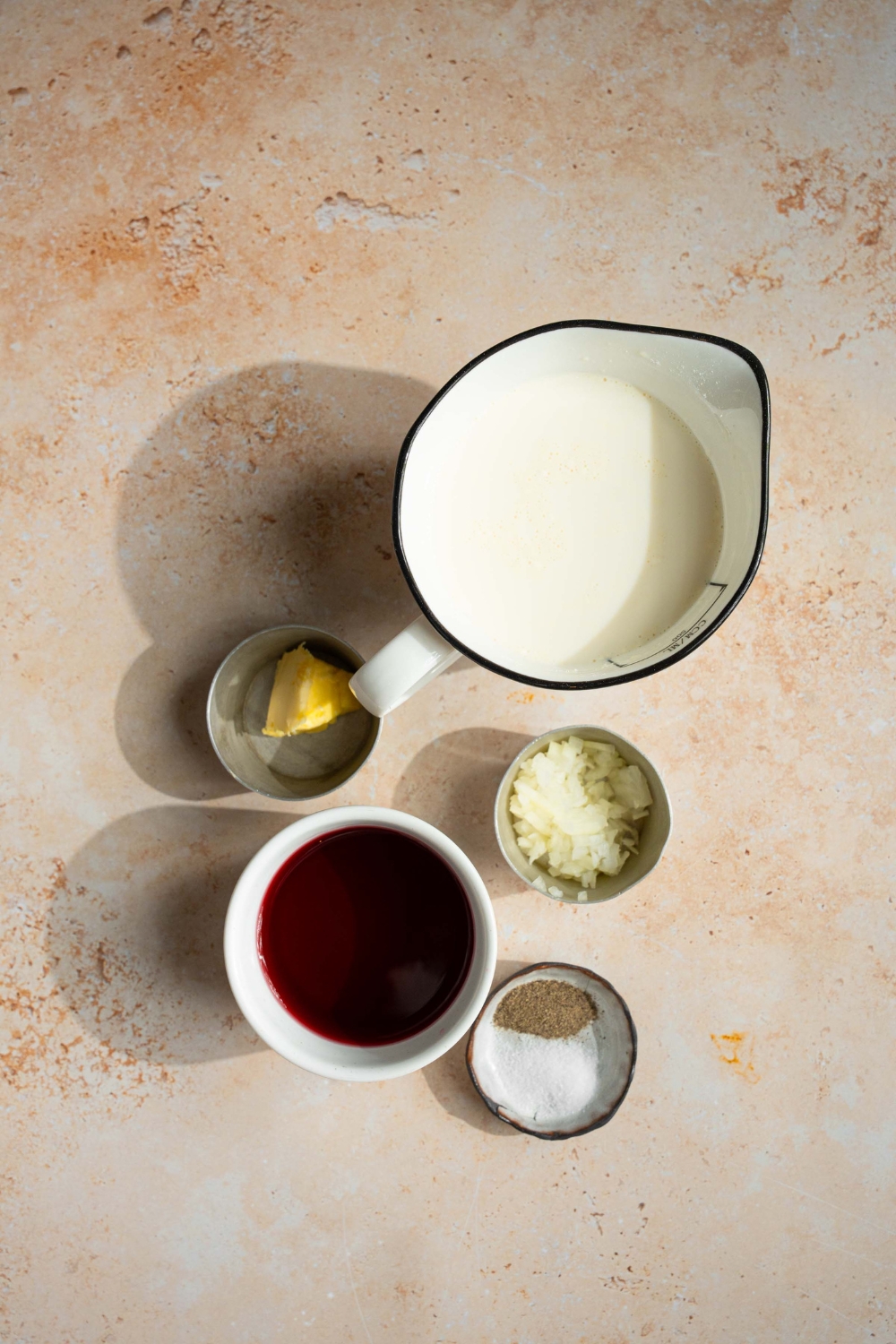 An overhead shot of several bowls in various sizes containing ingredients to make sherry cream sauce including sherry cooking wine, shallots, heavy cream, butter, and seasonings.