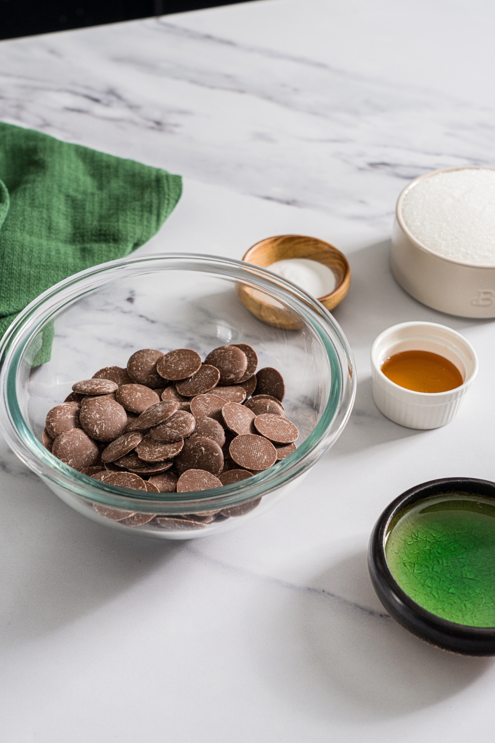 A marble counter with ingredients to make sponge candy including a bowl of milk chocolate, honey, sugar, baking soda, and corn syrup.