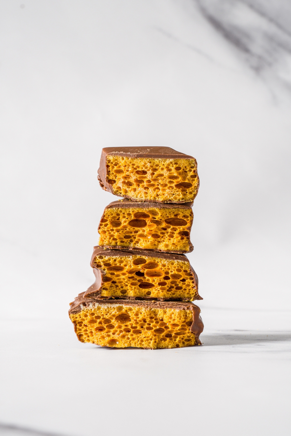 A marble counter with a two pieces of sponge candy sliced in half and stacked on top of one another.