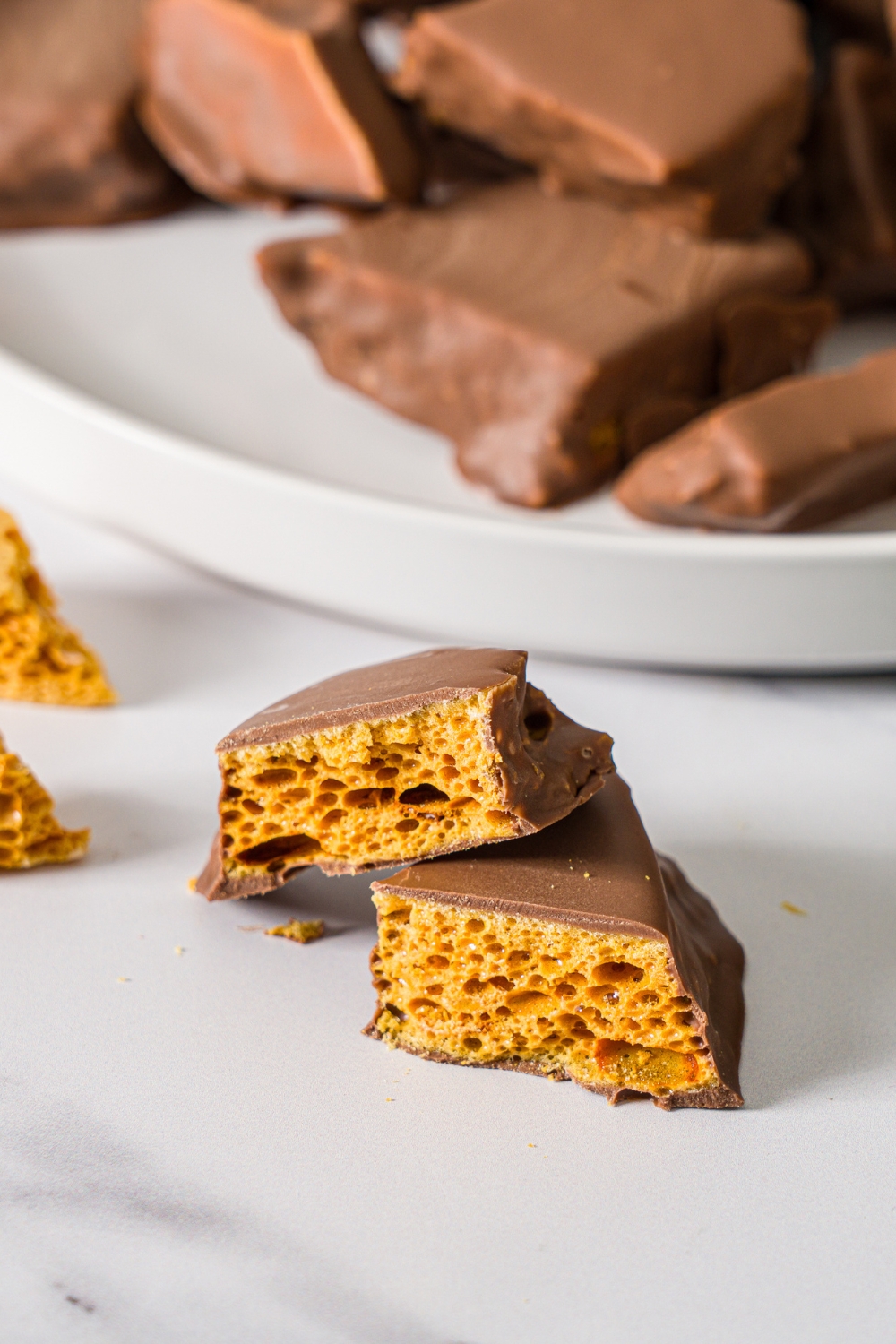 A marble counter with a white plate of sponge candy on a marble counter with a piece of sponge candy sliced in half.