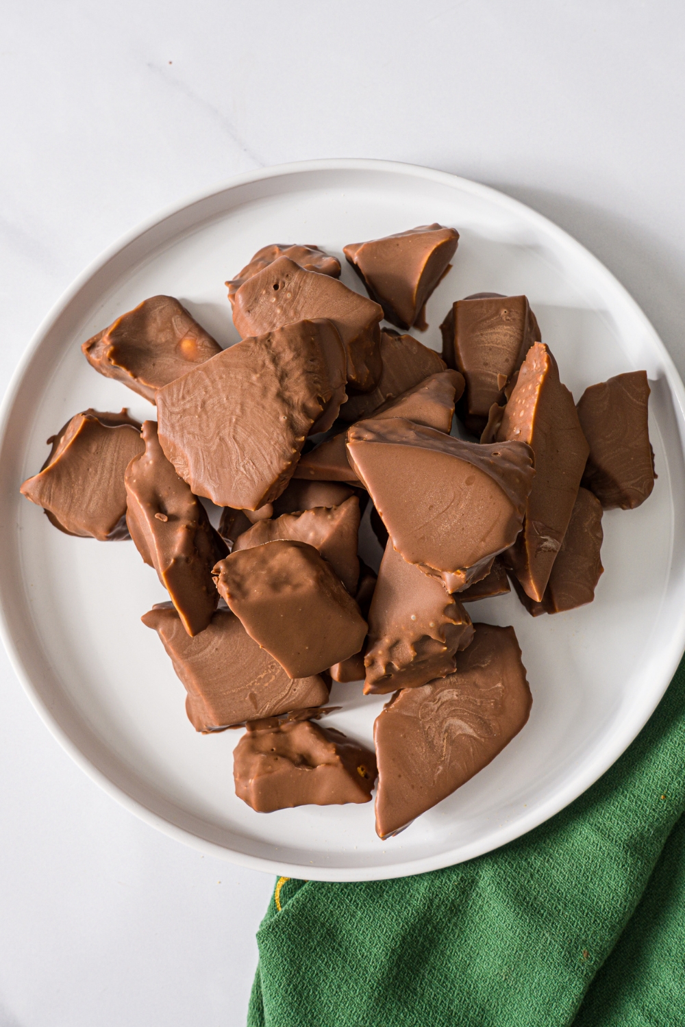 A white plate with milk chocolate sponge candy on a marble counter with a green cloth napkin.