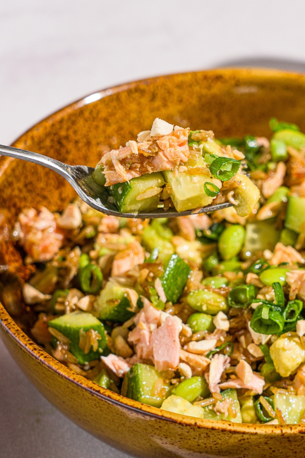 A bowl of crispy rice salmon salad garnished with sliced green onion. There is a fork with a bite of salad.