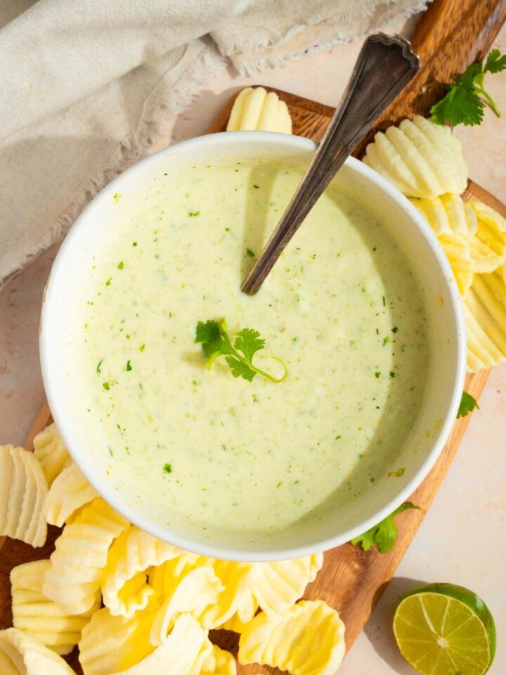 A white bowl filled with Chuy's creamy jalapeno dip on a wooden board with chips around it.