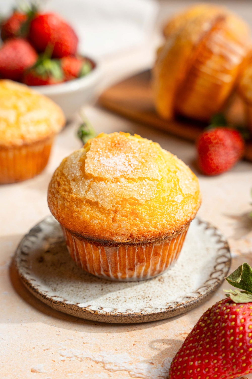 A vanilla muffin on top of a small round white plate. There are two more vanilla muffins behind it.