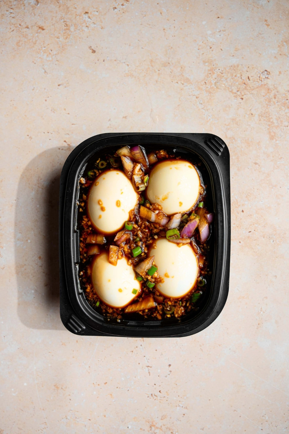 Four Korean marinated eggs, soaking in the marinade in a black container.