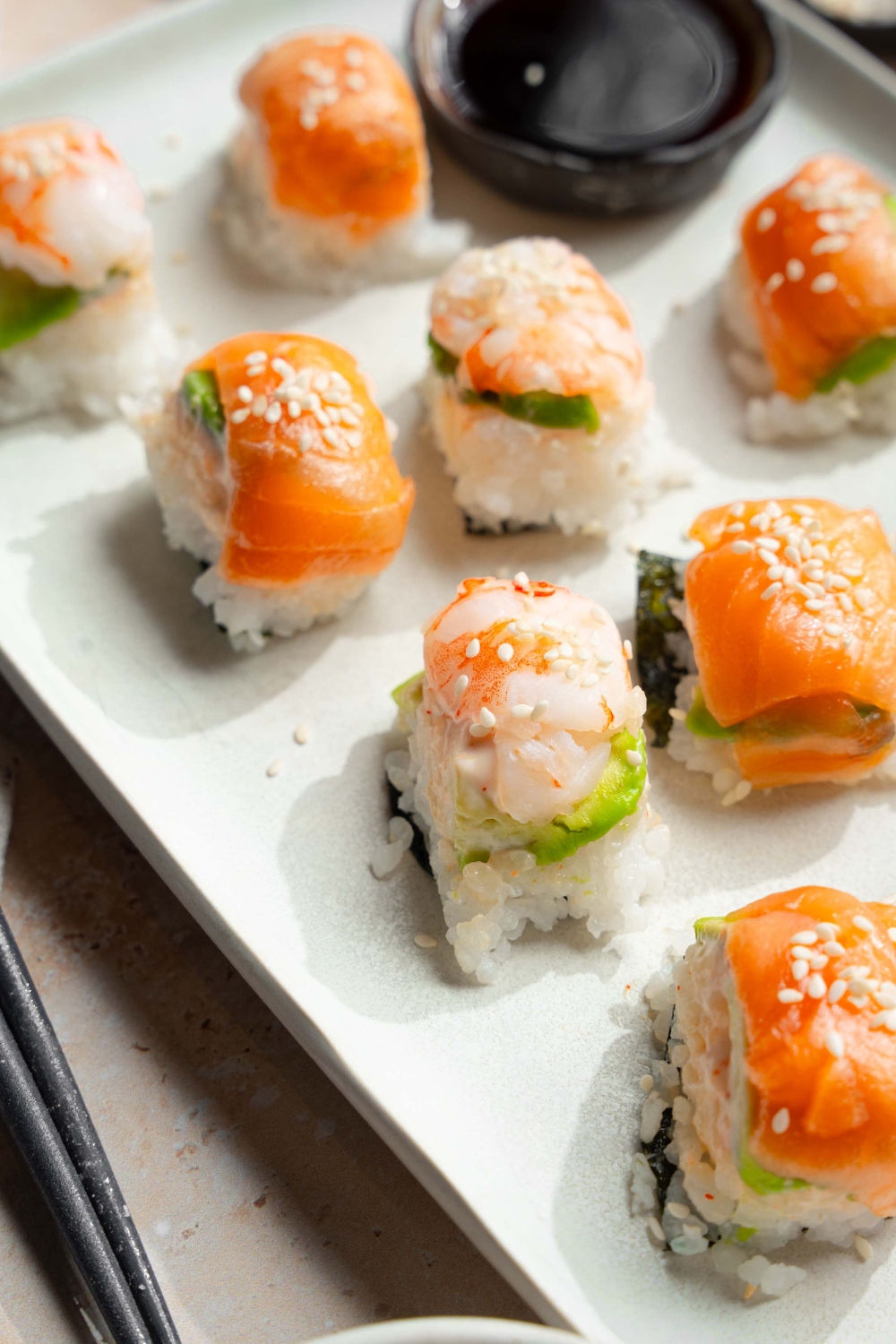 A bunch of pieces of ice cube tray, sushi on a white tray with cup of soy sauce.