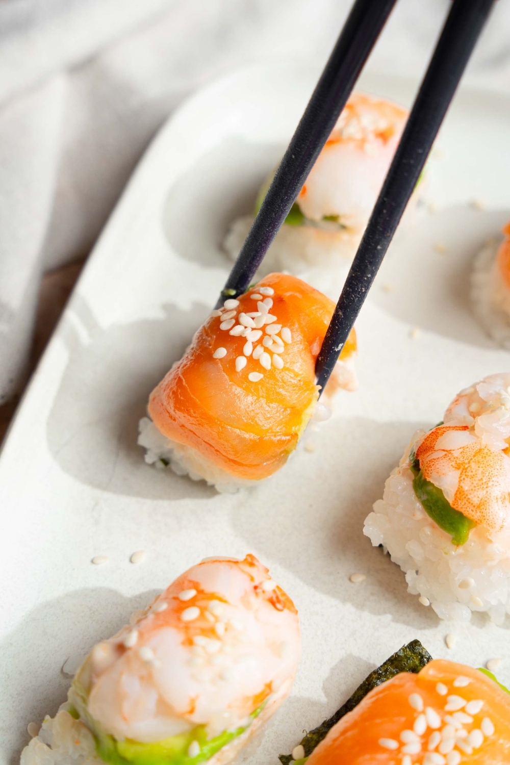 Chop sticks pinching a piece of sushi that's on a white plate.