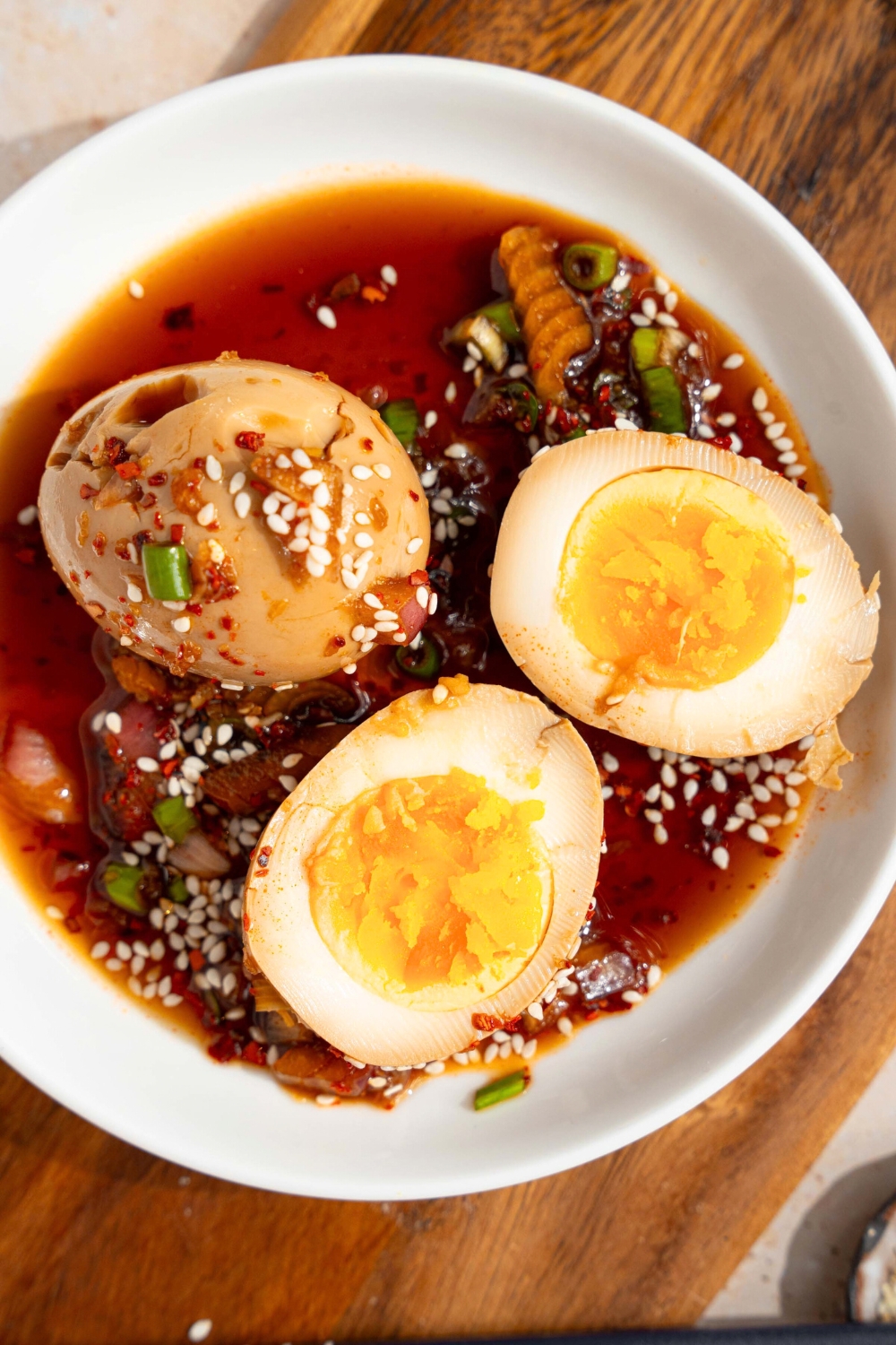 A Korean marinated egg and a sliced curry and marinated egg with the yolks, showing in the soy sauce, marinade and a white bowl.