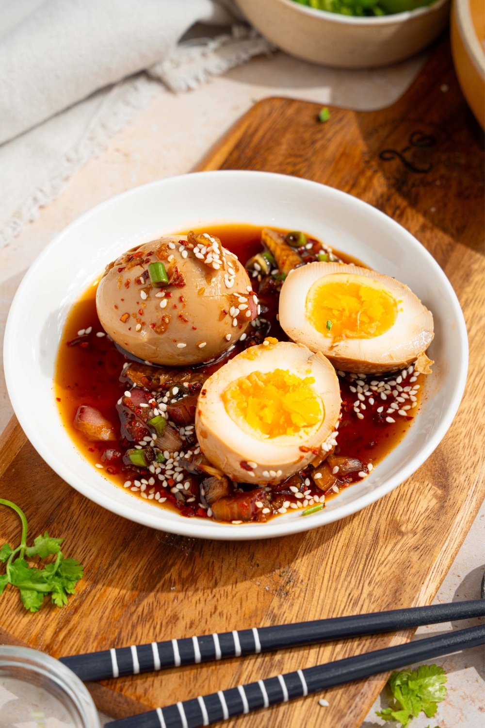 A whole mayak egg and a sliced mayak egg in a white bowl that is filled with the soy sauce marinade on top of a wood board.