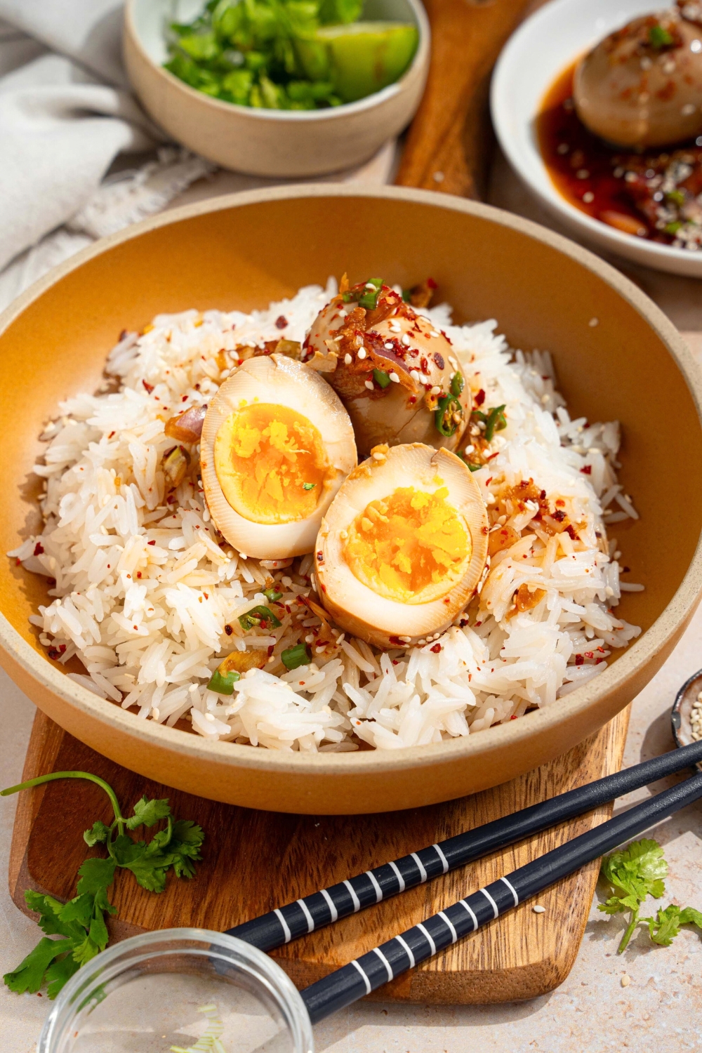 A sliced mayak egg with a whole mayak egg behind it on a bed of white rice in a bowl.