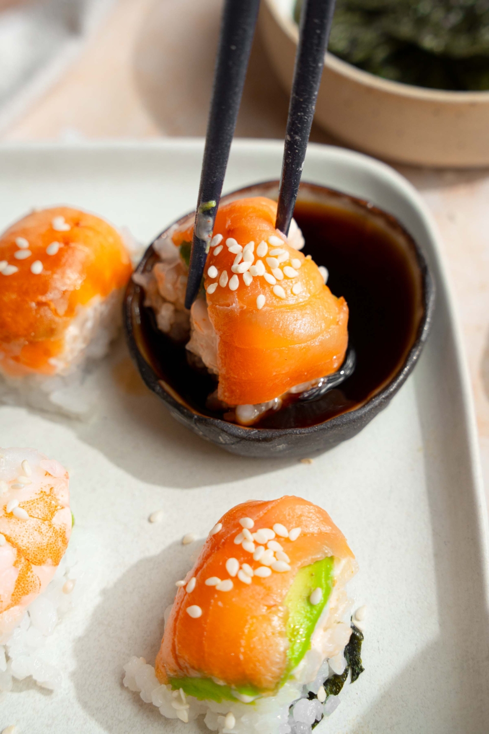 A piece of sushi being held by chop sticks over soy sauce.