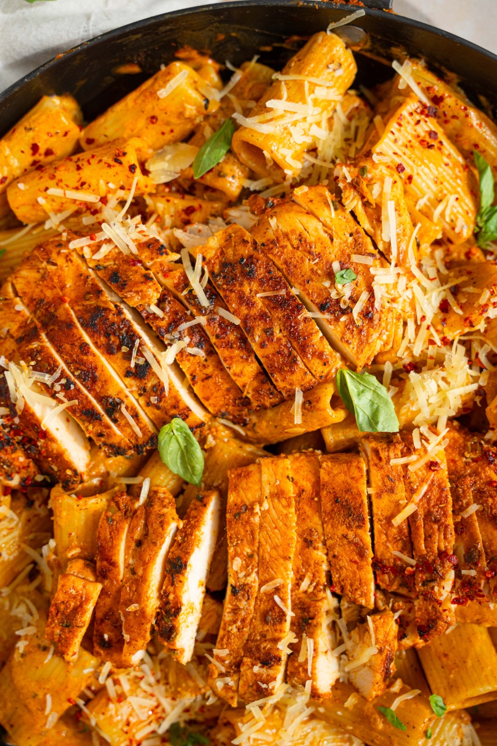 A skillet with garlic parmesan chicken pasta garnished with fresh bail, shredded parmesan and red pepper flakes.