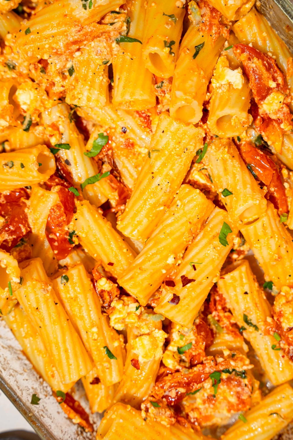 A glass baking dish with baked feta pasta garnished with fresh parsley and crushed red pepper.
