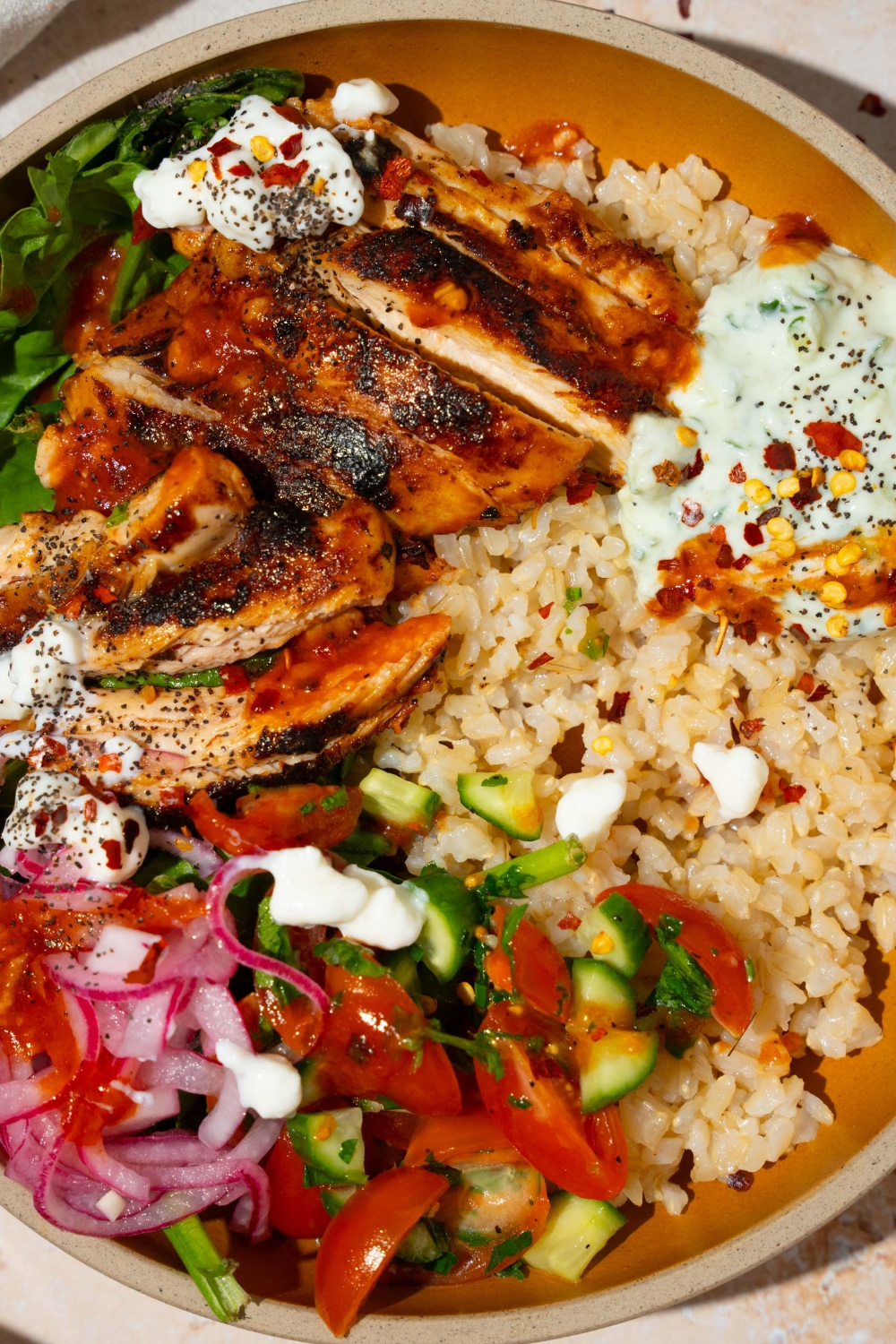 A bowl with Cava mediterranean bowl including rice, sliced marinated chicken, mixed greens, tzatziki, cucumber and tomato salad, and feta cheese in a harissa honey vinaigrette.