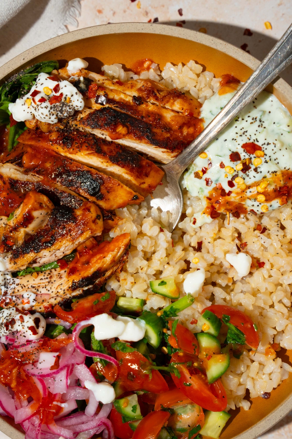 A bowl with Cava mediterranean bowl including rice, sliced marinated chicken, mixed greens, tzatziki, cucumber and tomato salad, and feta cheese in a harissa honey vinaigrette. There is a fork in the bowl.