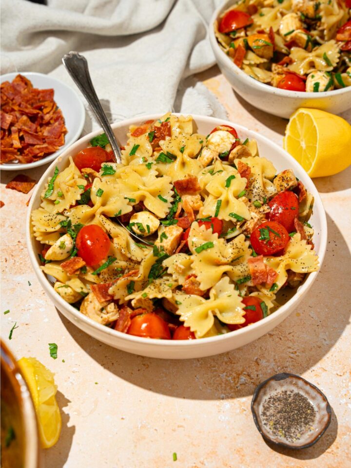 Chicken bruschetta pasta with bacon, tomatoes, and feta in a white bowl on top of a white counter.