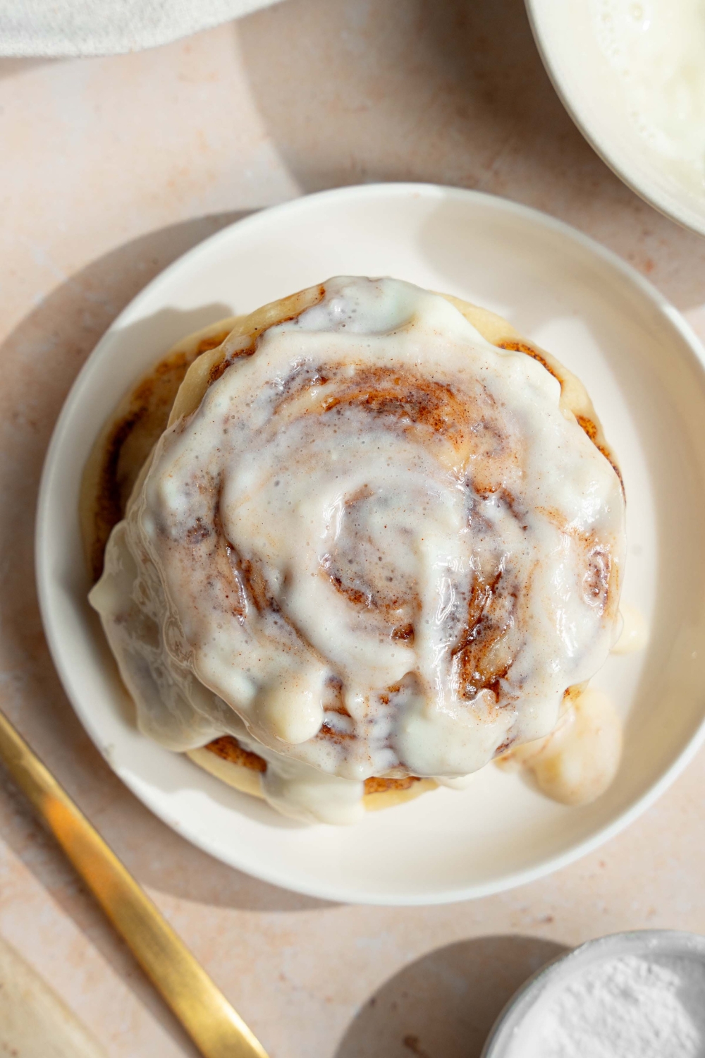 A white plate with a stack of cinnamon roll pancakes topped with cream cheese icing. The plate is on a tan counter with a fork.