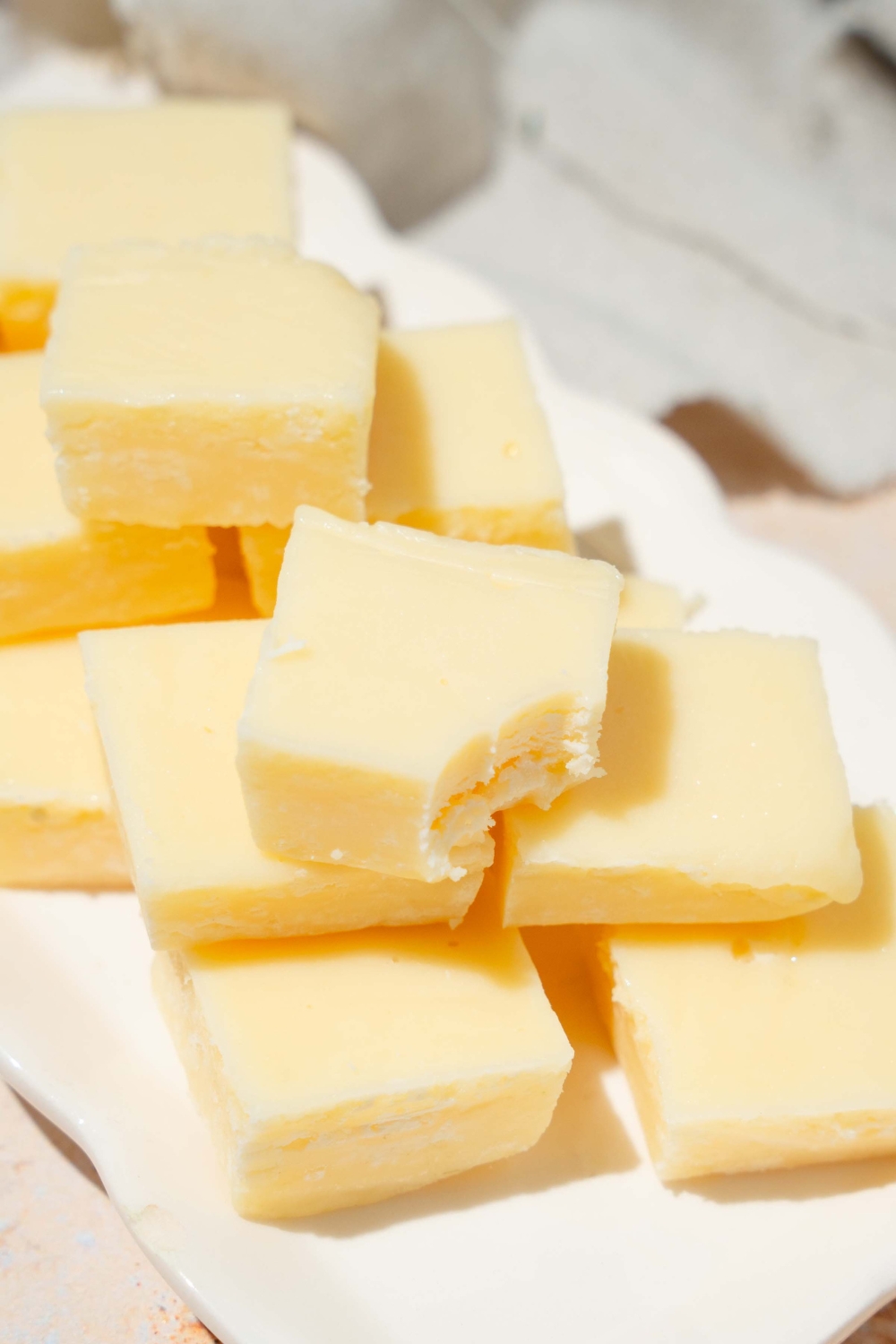 A white tray with pieces of vanilla fudge. A bite is taken from one of the pieces. The tray is on a tan counter with a white cloth napkin.