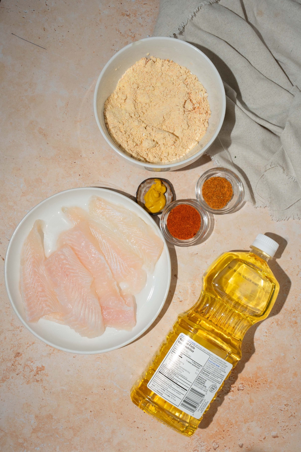 An overhead shot of several bowls in various sizes for southern style fried fish including fresh whiting, mustard, seasoned fish fri mix, cajun seasoning, old bay seasoning, and oil.