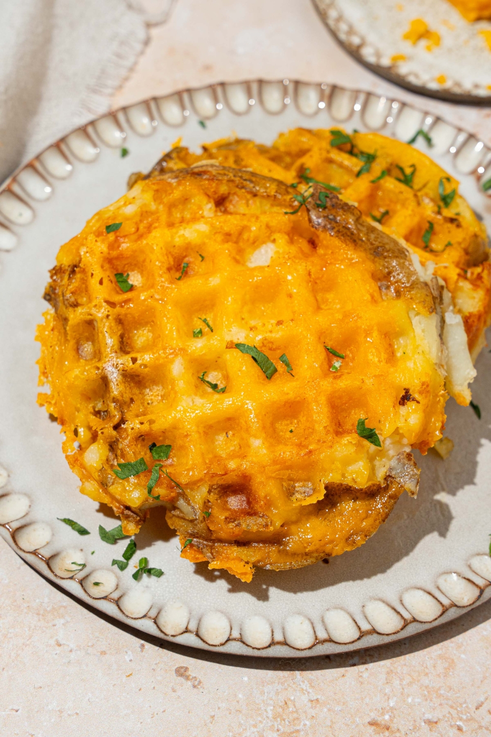 A white plate with two crispy waffle potatoes garnished with herbs. The plate is on a tan counter.