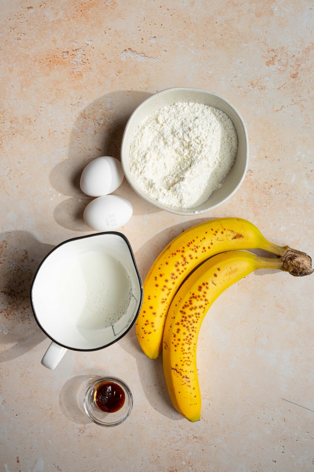 An overhead shot of ingredients to make banana pancakes including a banana, pancake mix, eggs, milk, and vanilla.