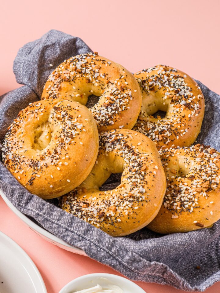 A bowl of greek yogurt everything bagels. The bowl is lined with a blue cloth napkin. The bowl is on a pink counter.