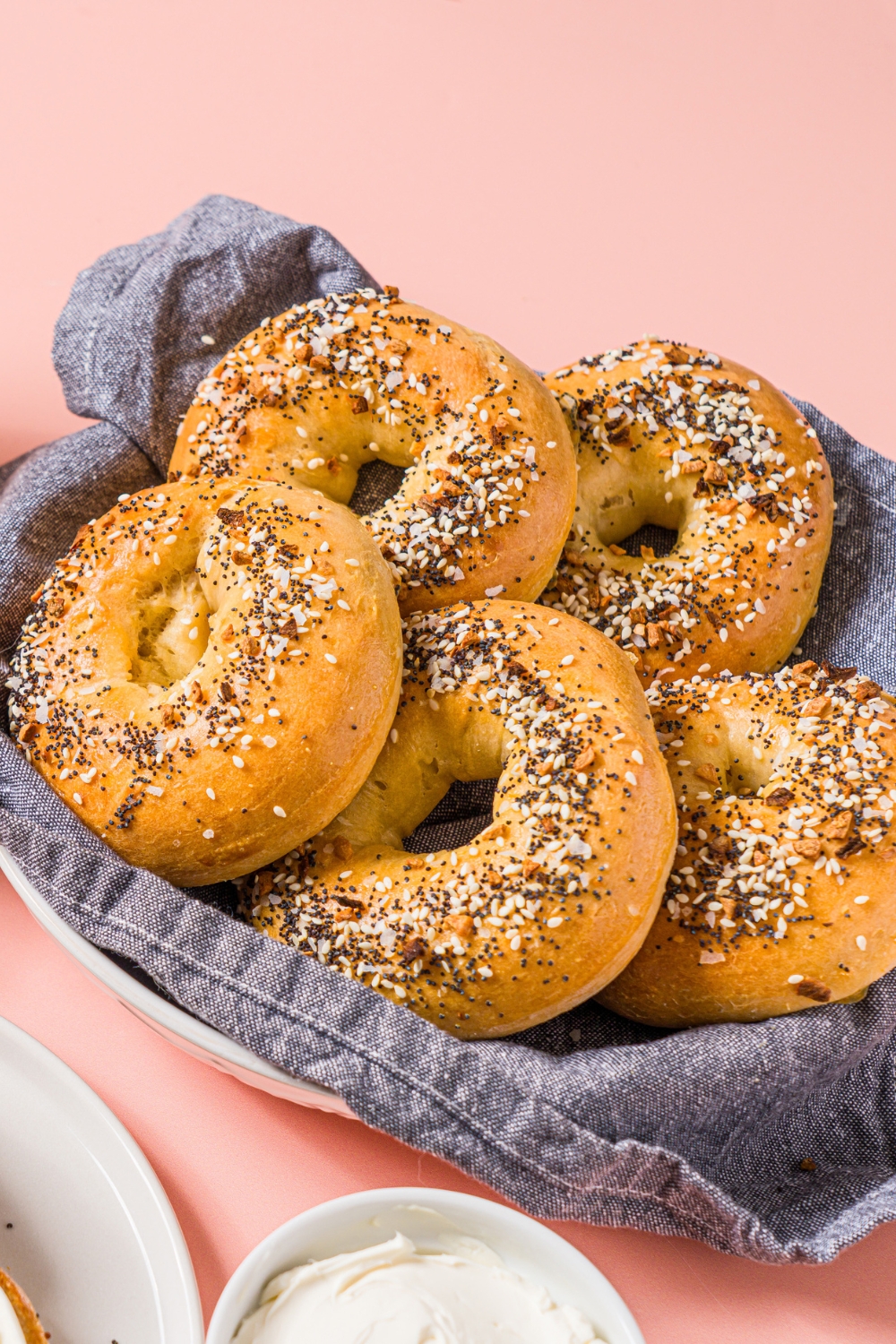 A bowl of greek yogurt everything bagels. The bowl is lined with a blue cloth napkin. The bowl is on a pink counter.