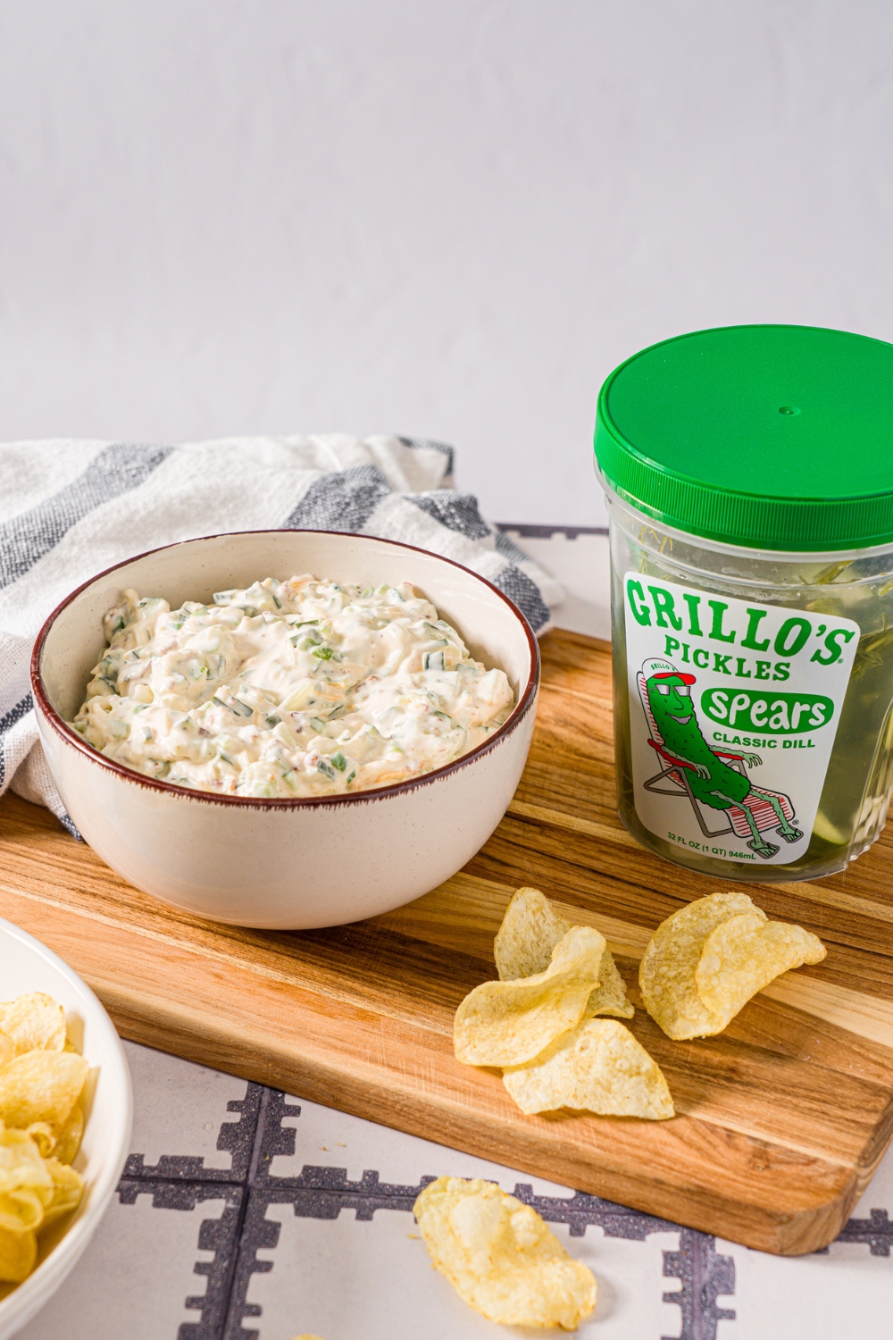 A tub of Grillo's pickles with a white bowl that is filled with Grillo's pickle dip next to it.