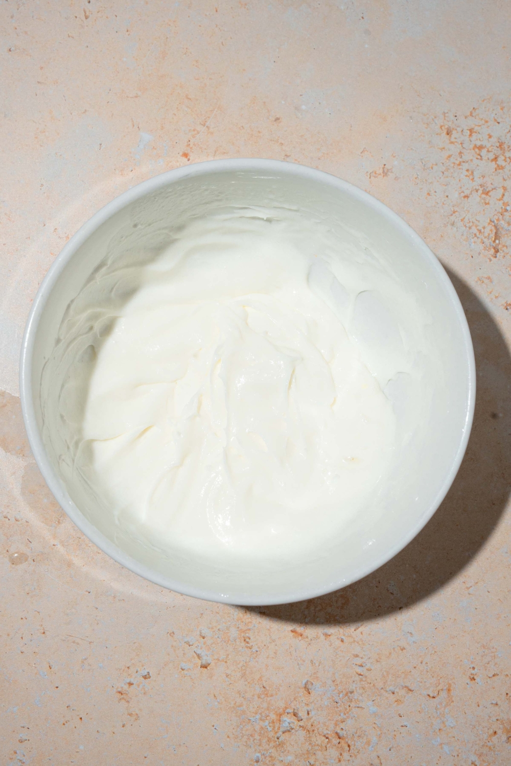 A white bowl with whipped cream. The bowl is on a tan counter.