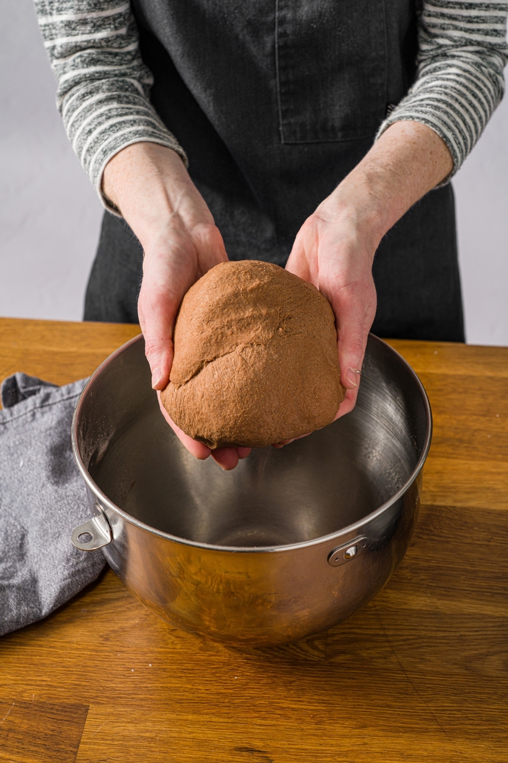 Hands holding a ball of Outback sweet molasses brown bread dough over a large mixing bowl. The bowl is on a wooden board.
