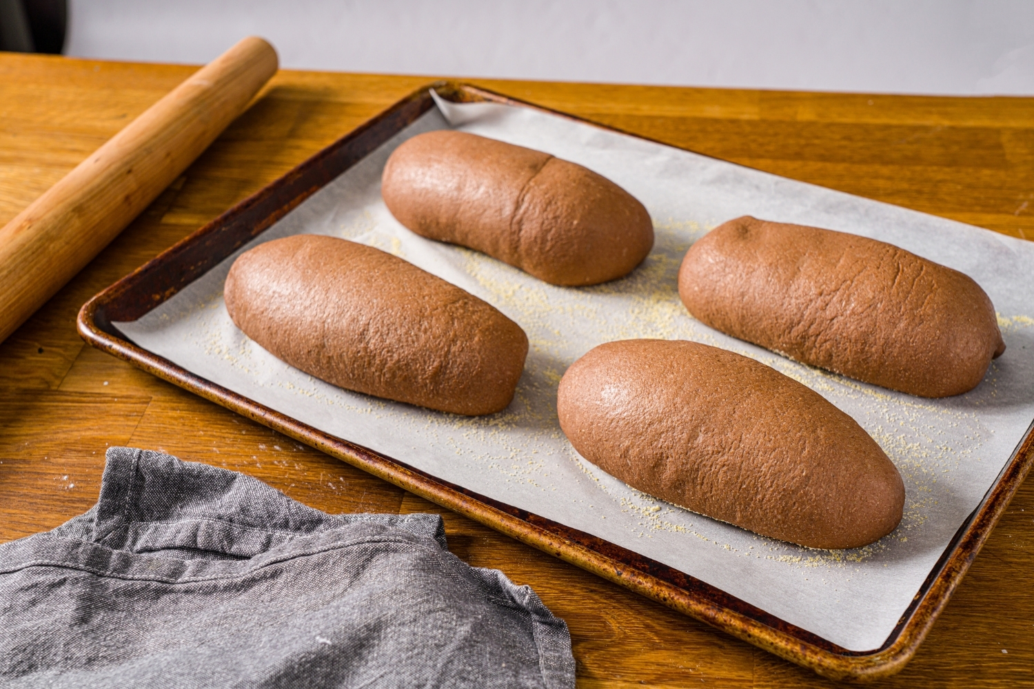 A baking sheet lined with parchment paper with four baked Outback sweet molasses brown bread loaves. The sheet is on a wooden counter with a blue cloth napkin.