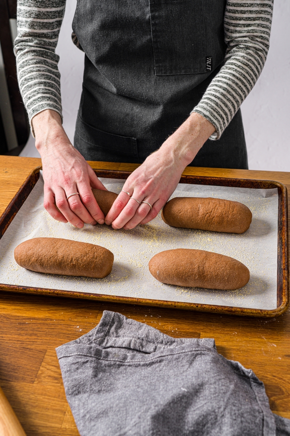 A hand shaping Outback sweet molasses brown bread dough loaves on baking sheet lined with parchment paper. The sheet is on a wooden counter.