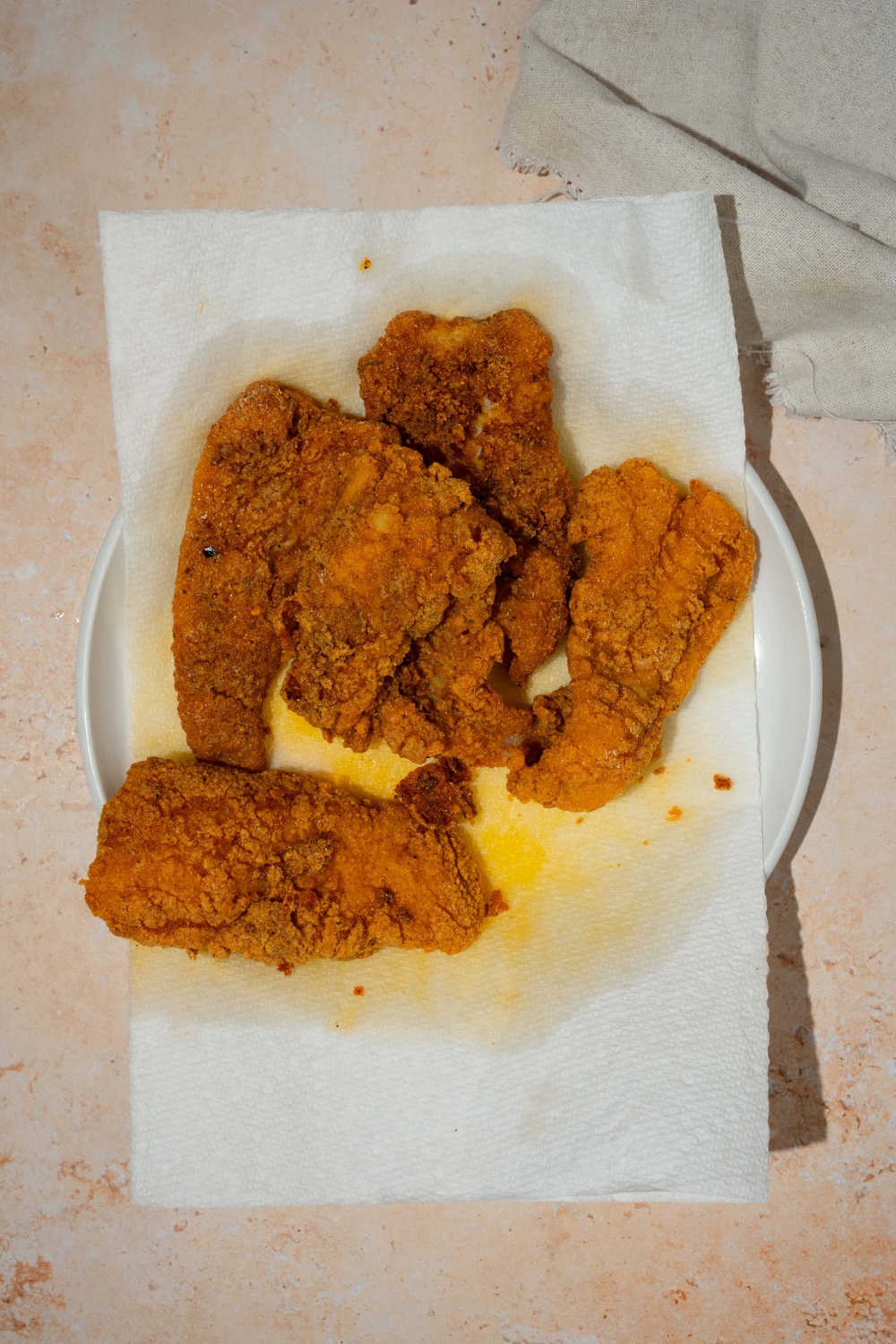 A white plate lined with paper towels with several pieces of fried fish. The plate is on a tan counter.