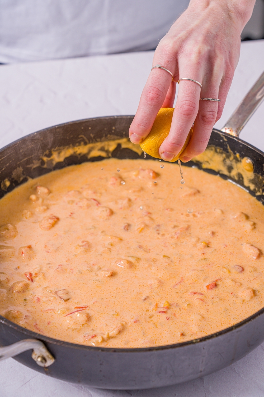 A skillet with Trader Joe's lobster bisque pasta sauce with lemon being squeezed into the sauce. The skillet is on a marble counter.