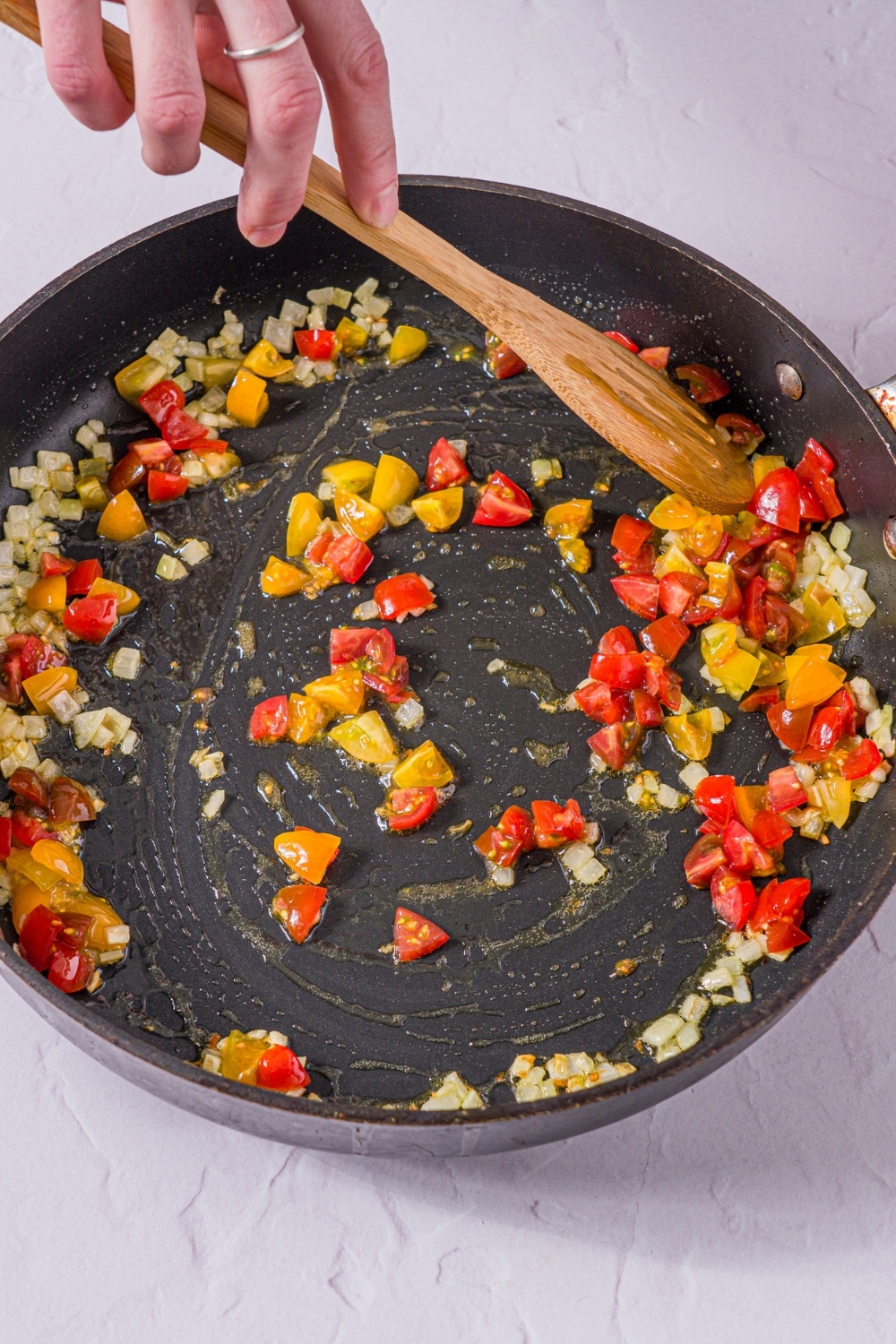 A skillet with diced tomatoes and onions sautéed in oil. The skillet is on a tan counter.