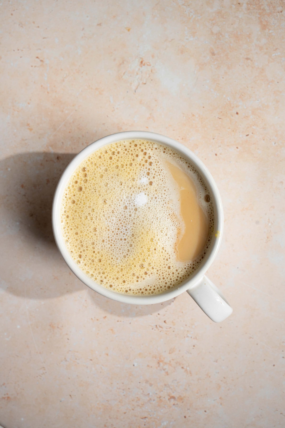 A white mug with Vietnamese egg coffee. The mug is on a tan counter.