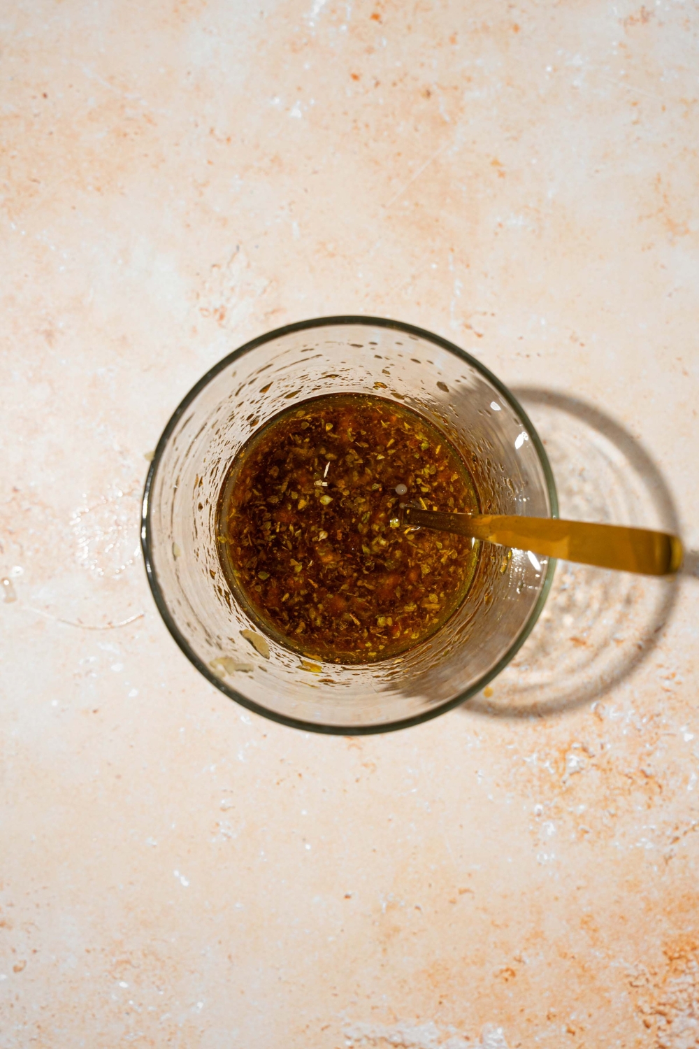 A small glass bowl with a spoon mixing balsamic vinaigrette. The bowl is on a tan counter.