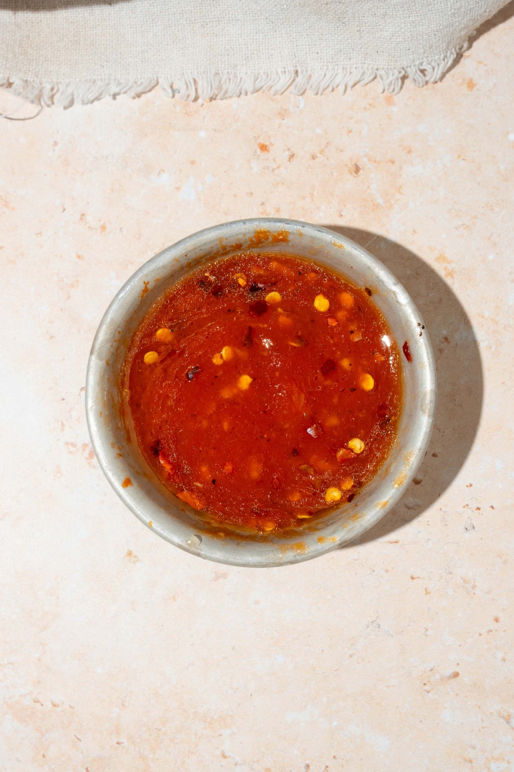 A small bowl with harissa honey vinaigrette. The bowl is on a tan counter.
