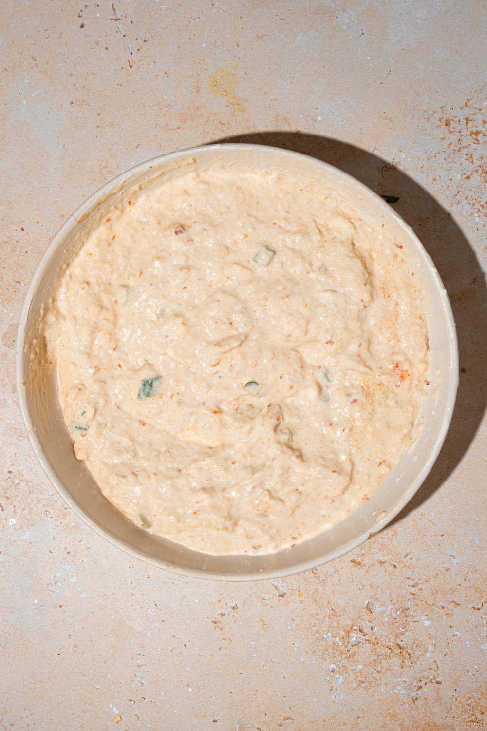 A white bowl with a crab rangoon dip mixture including crab meat, mayo, cream cheese, sour cream, and seasonings. The bowl is on a tan counter.