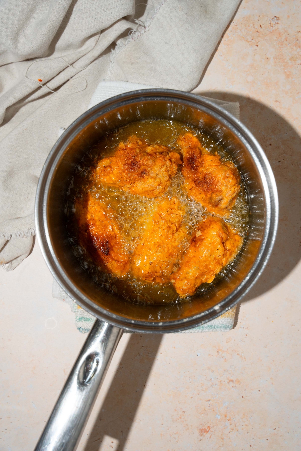 A pot with breaded chicken wings frying in oil. The pot is on a tan counter with a white cloth napkin.
